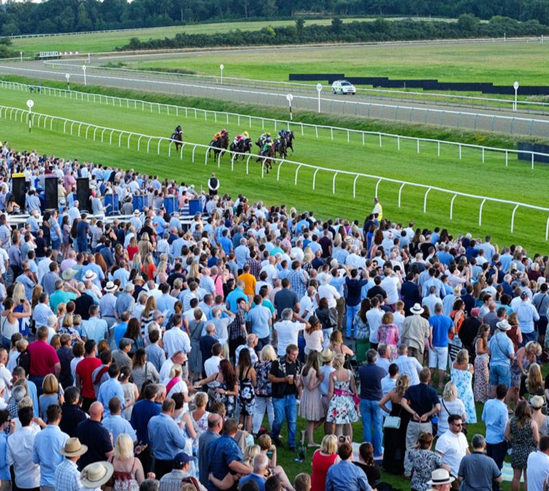 Crowds watching a group of jockeys racing towards the finishing post.