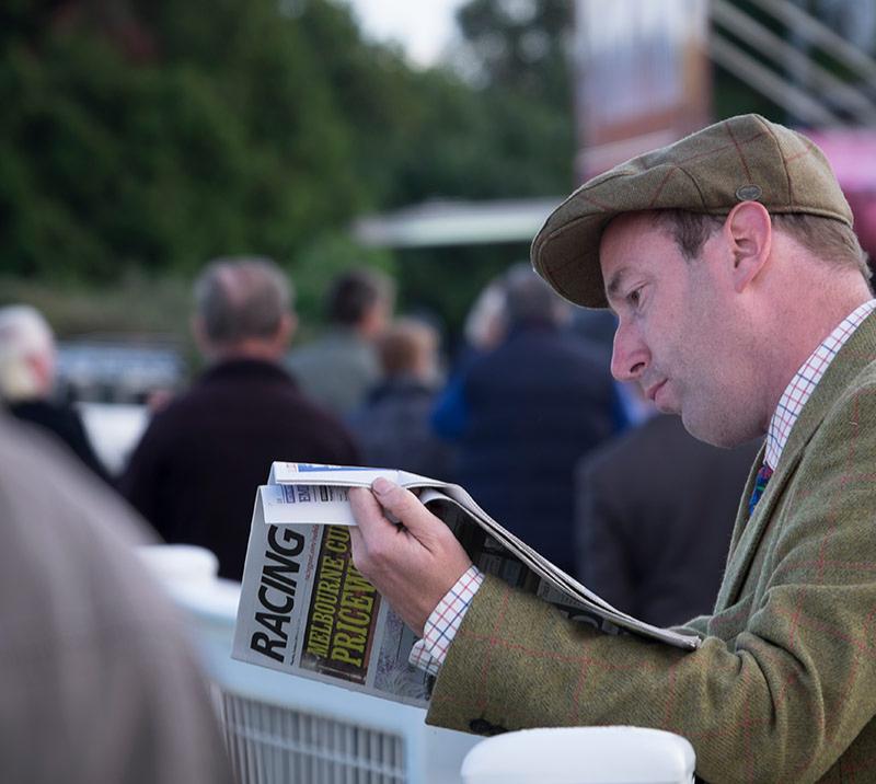 Racegoer reading through Racing Post newspaper.