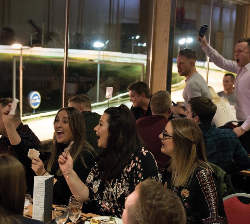 A crowd enjoy a trackside dinner whilst watching live greyhound racing.