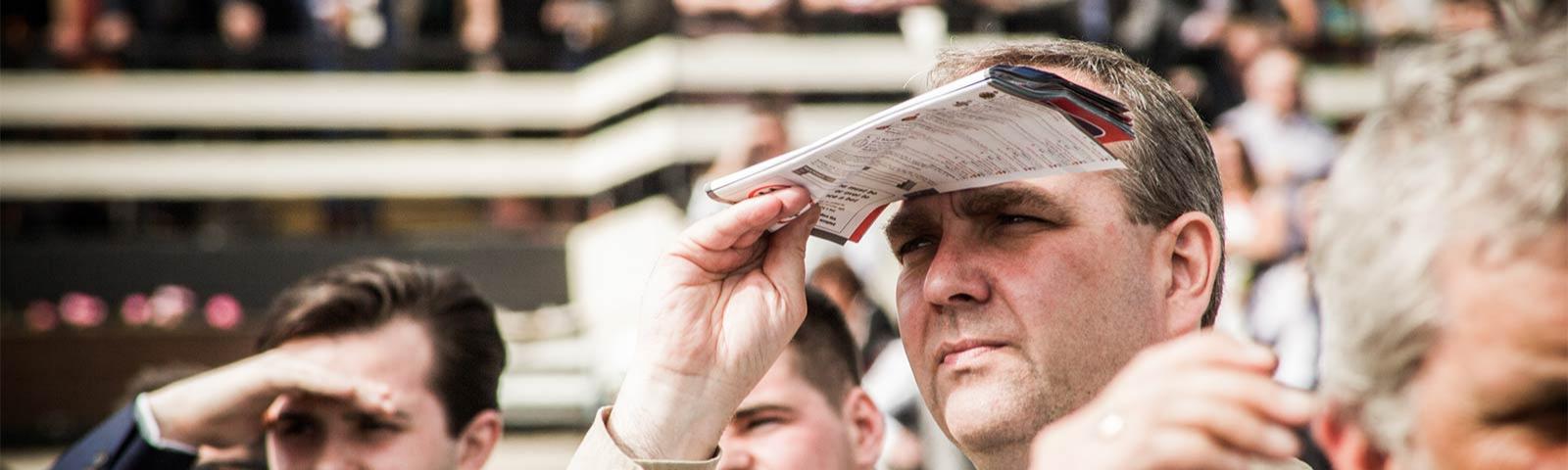 Gentleman shielding his eyes from the sun while watching racing.